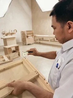 Worker assembling a wooden furniture component with a hand tool.