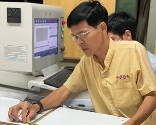 Factory worker inspecting a wooden panel beside computerized equipment.