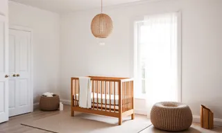 Wooden baby crib with rattan pendant, pouf and basket in a bright room.