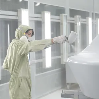 Worker in protective clothing spray-finishing a white furniture component