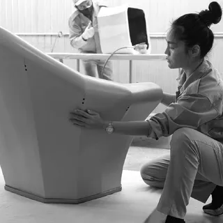 Worker inspecting a large white molded furniture component in a workshop