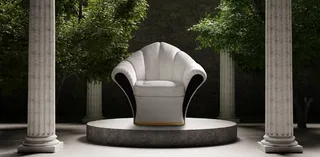 White sculptural armchair displayed on a circular plinth between stone columns
