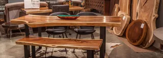 Live-edge wooden dining table and bench with chairs in a furniture showroom.