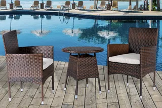 Woven outdoor dining chairs and round table beside a swimming pool