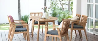 Outdoor wooden dining table and chairs arranged on a covered patio.