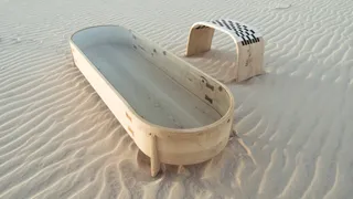 Curved wooden tub with a matching arched stool on sand