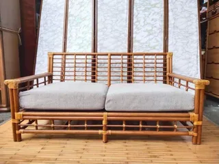 Front view of a bamboo sofa with two light fabric seat cushions.