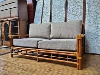 Bamboo-framed sofa with two gray cushions in an interior.