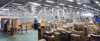 Large furniture factory floor with workers, machinery and stacked wooden components.