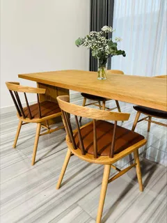Wooden dining table with curved-back chairs and a flower vase.
