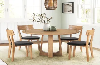 Round wooden dining table with four chairs in a bright dining room
