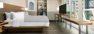 Hotel bedroom with a wood bed, desk, bench, television and large windows