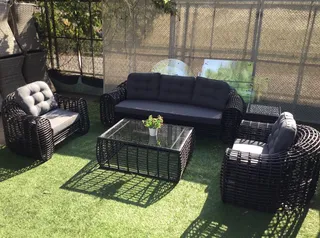 Black woven outdoor sofa, armchairs and glass coffee table on artificial grass