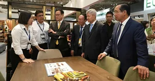 Representatives presenting a wooden dining table at a furniture trade show