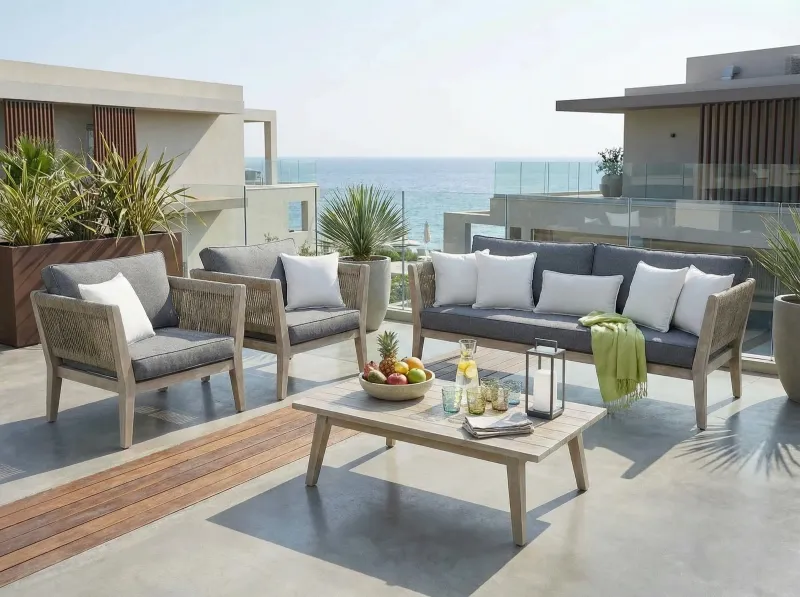 Outdoor woven seating set with cushions, coffee table and lounge chairs on a seaside terrace.