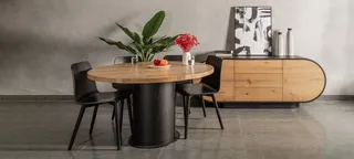 Round wood dining table with black chairs and a rounded wooden sideboard