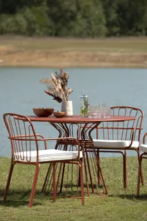 Rust-colored metal outdoor dining table and chairs with white cushions beside a lake