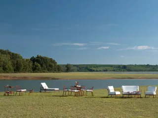 Collection of metal outdoor chairs, tables and loungers arranged beside a lake