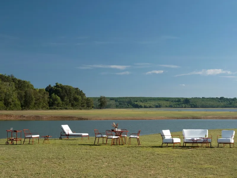 Collection of metal outdoor chairs, tables and loungers arranged beside a lake