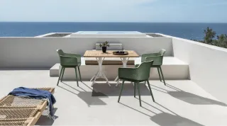Green outdoor chairs and a wooden table arranged on a seaside terrace