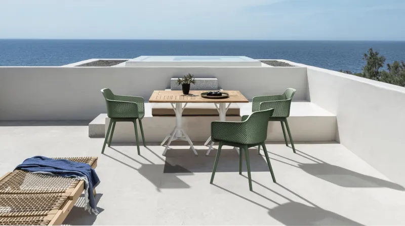 Green outdoor chairs and a wooden table arranged on a seaside terrace