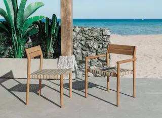 Two wooden outdoor chairs with woven seats near a beach