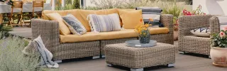 Wicker outdoor sofa, armchairs and ottoman arranged on a patio.