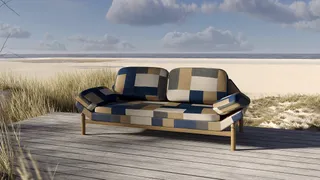 Patchwork upholstered sofa on a wooden deck beside a sandy beach