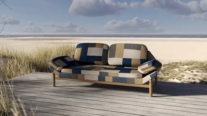 Patchwork upholstered sofa on a wooden deck beside a sandy beach