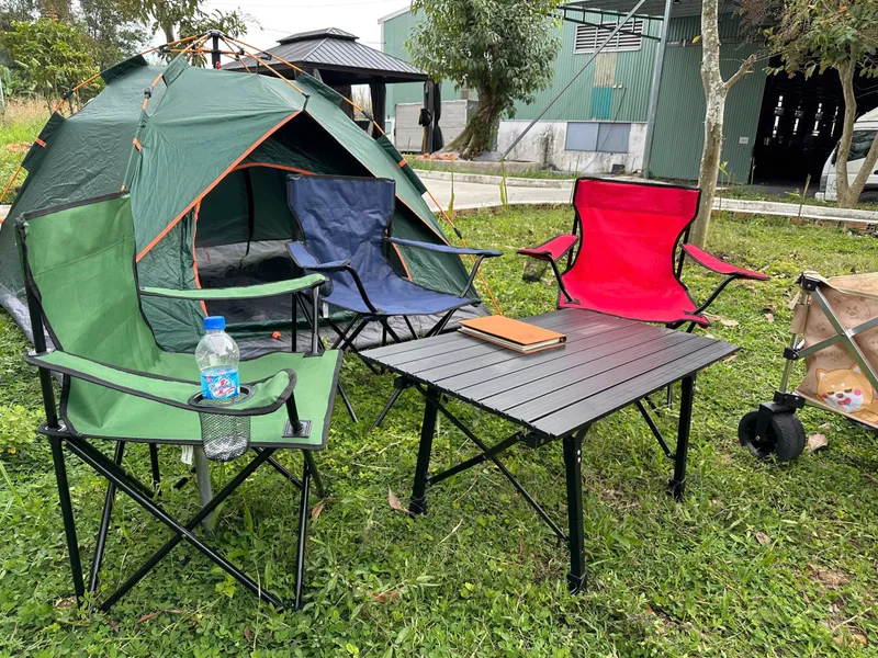 Outdoor camping setup with tent, folding chairs and slatted table