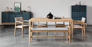 Wood dining table with chairs, bench and dark cabinets in a styled interior.