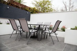 Outdoor dining table and four mesh chairs on a paved patio