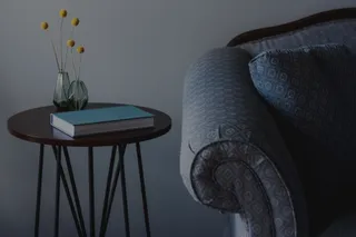 Upholstered patterned armchair beside a round wooden side table with books and vases.