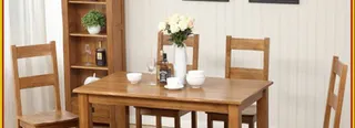 Wooden dining table set with four chairs, tableware and a flower vase.