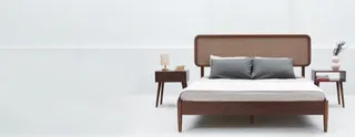 Wooden upholstered-headboard bed with matching bedside tables in a bright studio.