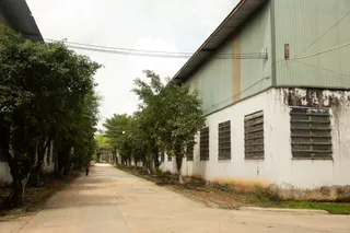Exterior of a corrugated industrial furniture workshop beside a tree-lined road.