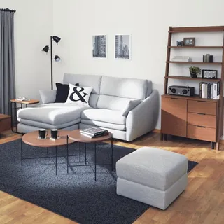Light gray sectional sofa and ottoman beside wooden shelving in a living room
