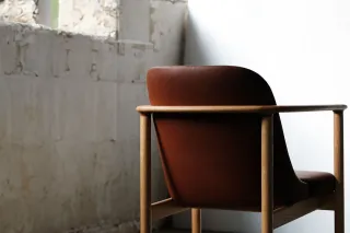 Brown leather armchair with a rounded wooden frame and slender arms.