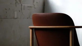 Wooden armchair with a rounded brown leather back and slim horizontal arms.