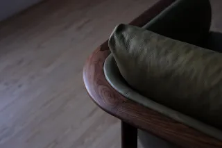 Close-up of a curved walnut chair back and wooden support on a concrete floor.
