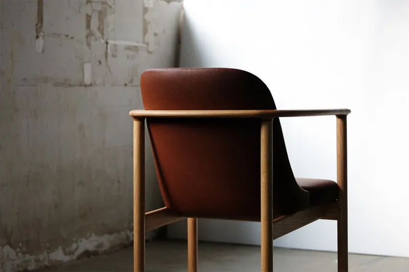 Brown leather armchair with a rounded wooden frame in a studio setting.