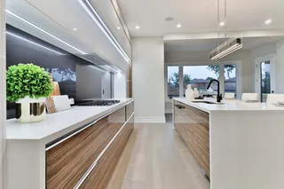 Contemporary kitchen with woodgrain cabinetry, white island and integrated lighting