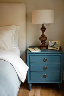 Blue three-drawer bedside cabinet beside a bed with a table lamp
