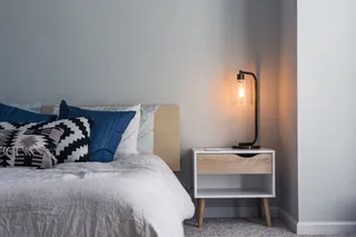White and wood bedside cabinet beside a bed with a wall lamp
