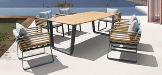 Outdoor wood-and-metal dining table with cushioned slatted armchairs by the sea.