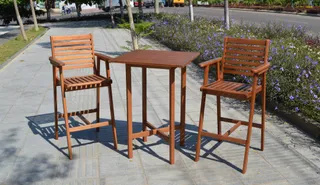 Wooden outdoor table with two matching folding bar chairs beside a landscaped road