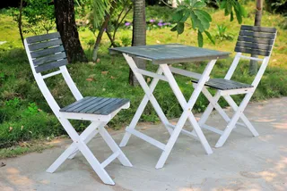 White folding outdoor table with two matching slatted chairs in a garden