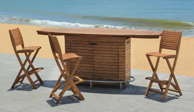 Wooden outdoor bar cabinet and four folding bar chairs on a beach