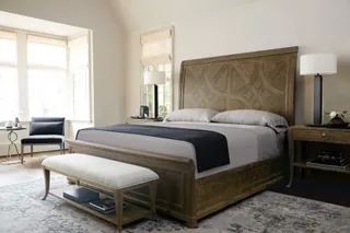 Carved wooden bed, bedside table, bench and armchair in a furnished bedroom