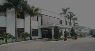 White factory building with palm trees, landscaped entrance and paved forecourt